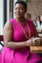 Woman in a pink dress with a gold wooden chain necklace by jianhui london and holding a mug in a casual setting.