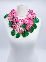 Floral necklace with pink flowers and green leaves on a mannequin against a white background