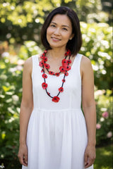 Woman in a white dress with a red necklace standing in a garden wearing Handmade Recycled Plastic Poppy Flower Necklace – Eco-Friendly Statement Jewelry
