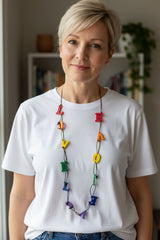 Person wearing a rainbow necklace handmade from recycled wood, LOVE letter shape perfect for Pride gift,  indoors