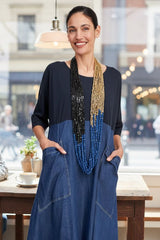 Woman wearing a blue dress with a beaded necklace in a casual setting.