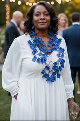 A woman standing outdoors at a social event, wearing a white long-sleeve dress and a bold royal blue geometric necklace made of recycled plastic water bottle by Jianhui London.