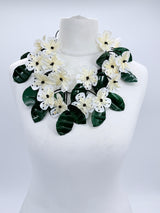 Floral necklace with green leaves and white flowers on a mannequin against a white background